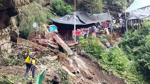 Rescue worker clearing debris after Uttarakhand Cloudburst, with people watching from a safe distance near damaged tents.